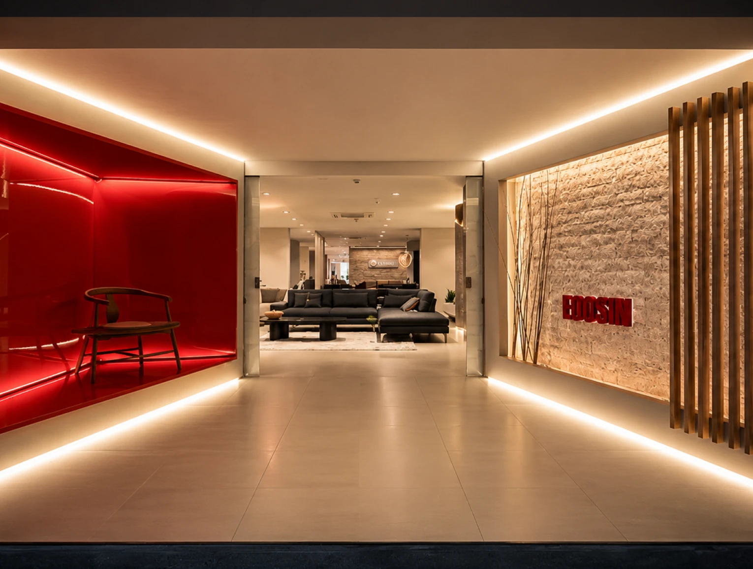 Entrada do showroom da EOOSIN: parede de pedra iluminada com o nome da marca em relevo vermelho, nicho laqueado e ripado de madeira.