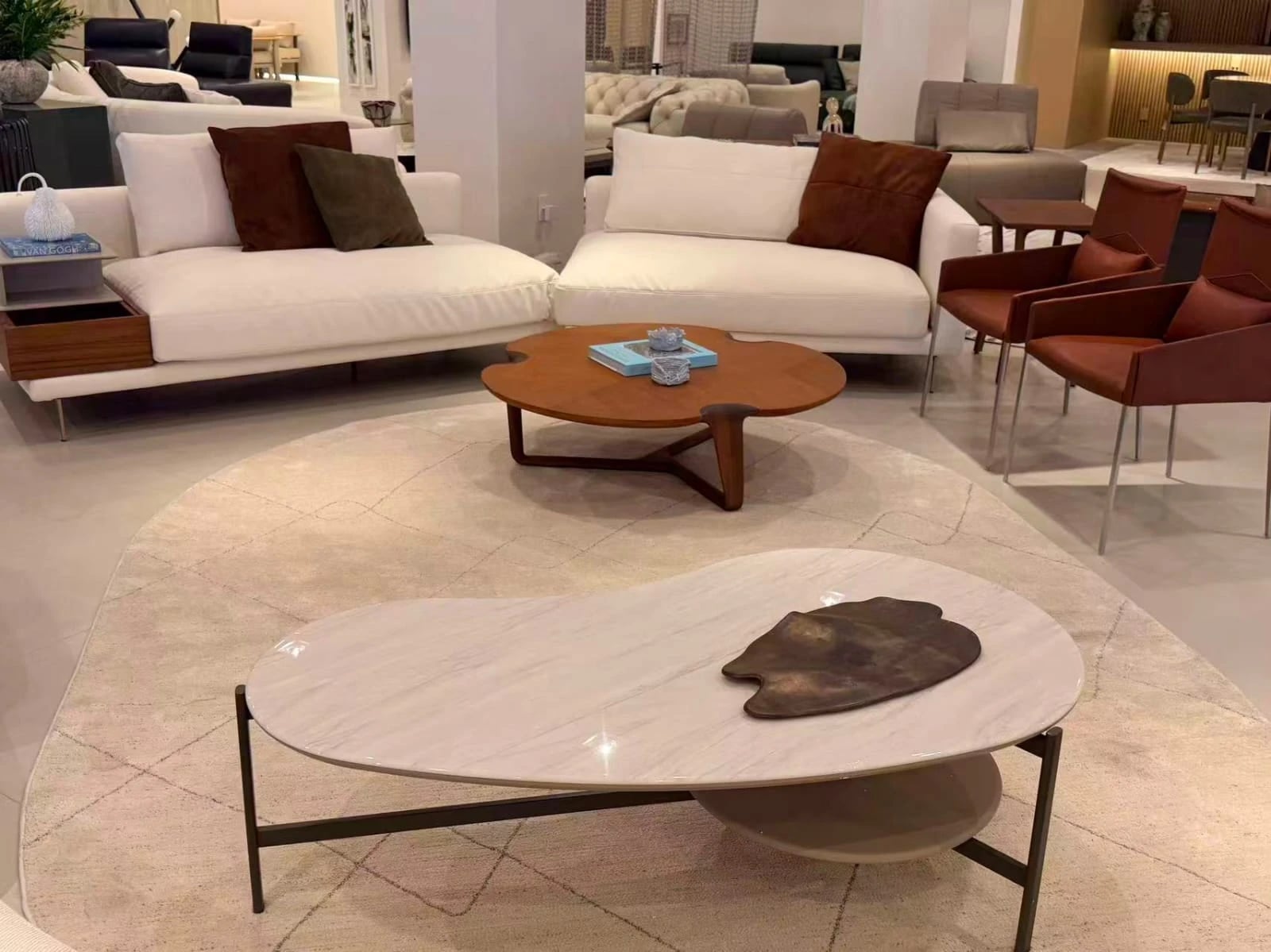 Sofás claros, mesa de centro em madeira e mesa de mármore de tampo orgânico, no showroom.